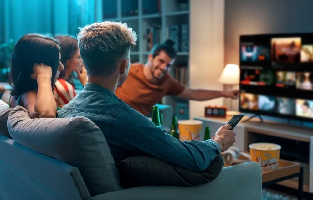 Freunde auf dem Sofa wählen einen Film aus der IPTV Senderliste auf dem Fernseher